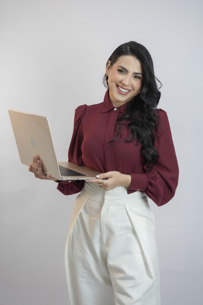 Andreza Lima de blusa vinho e calça branca segurando notebook em foto corporativa