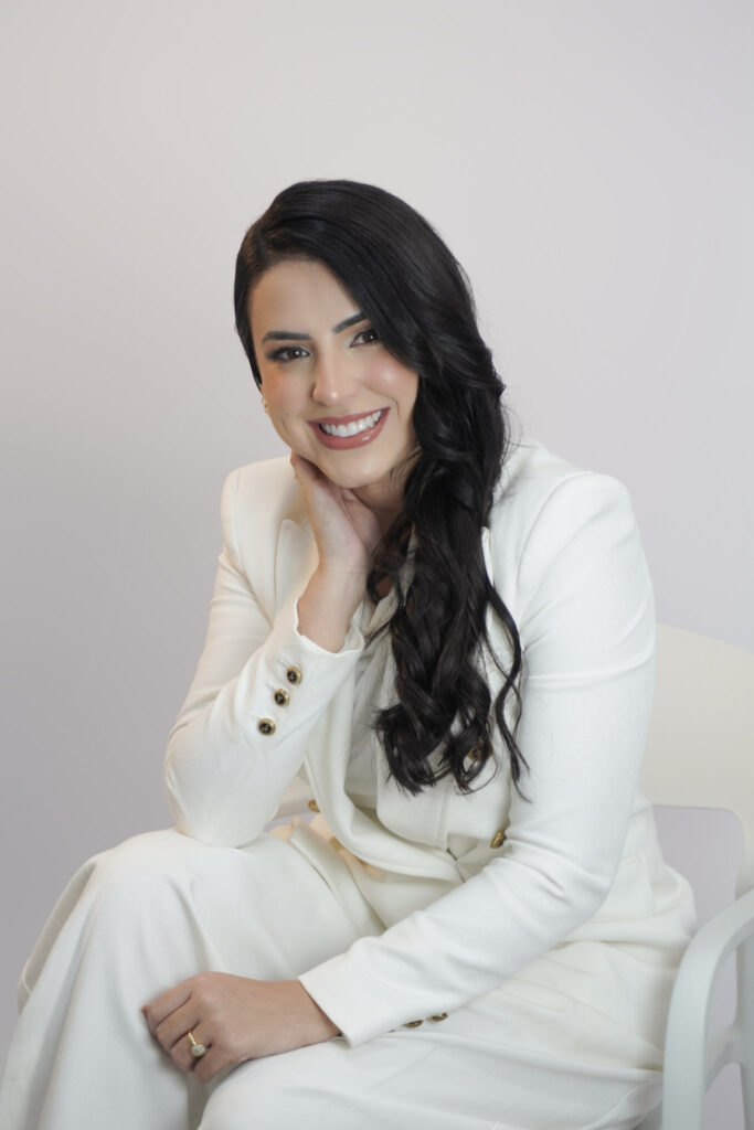 Andreza Lima sentada de terno branco com a mão no rosto em ensaio corporativo