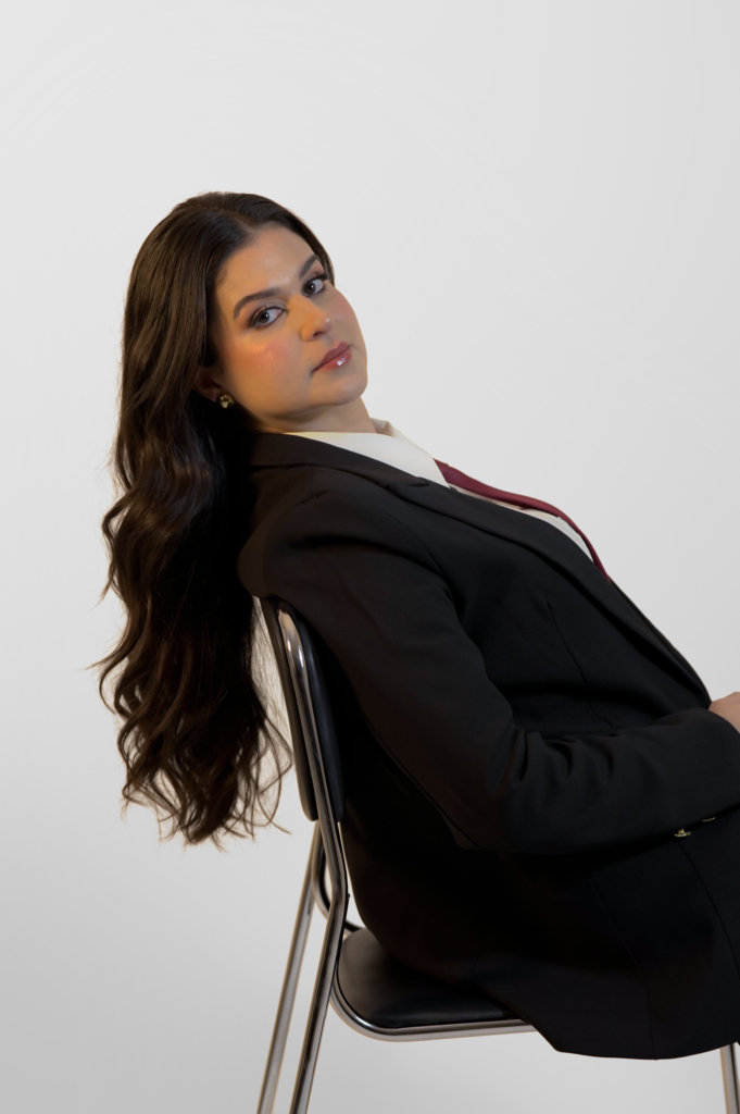 Ensaio corporativo para médica: Dra. Wilma Viviane de terno preto e gravata vinho sentada em fundo claro